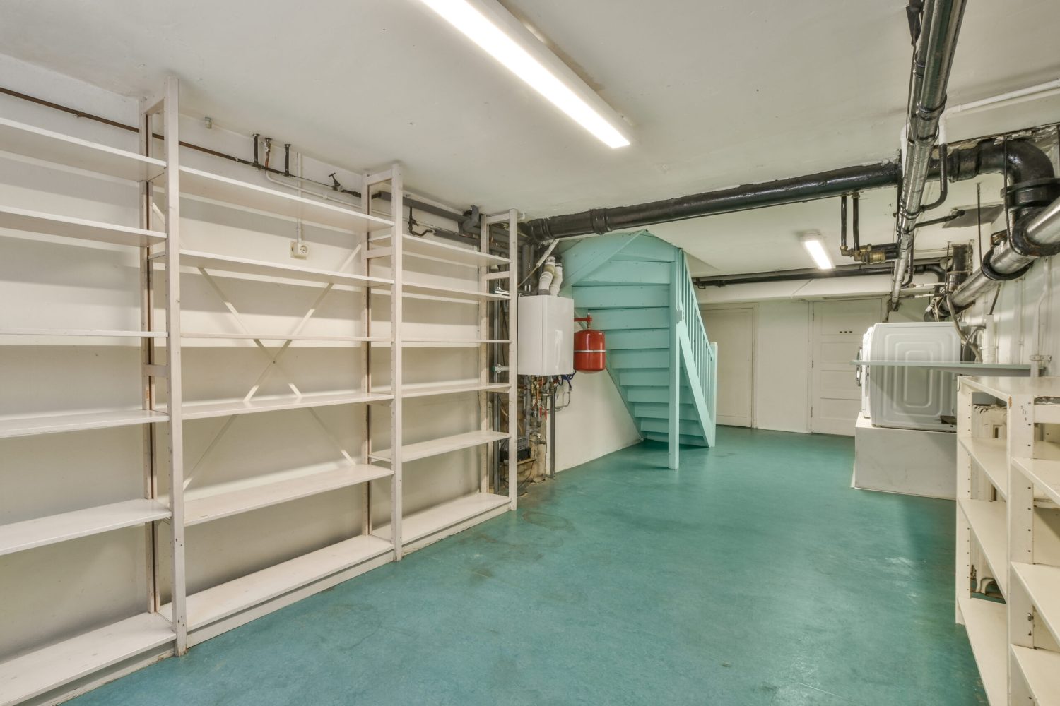 Boiler room of an apartment building with pipes and metering devices. A long room with engineering communications and with washing machine in the modern apartment