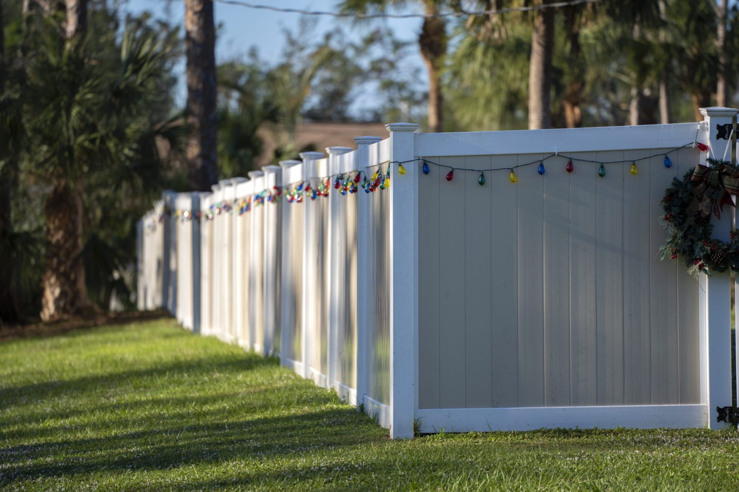 White vinyl picket fence on green lawn surrounding property grounds for backyard protection and privacy.